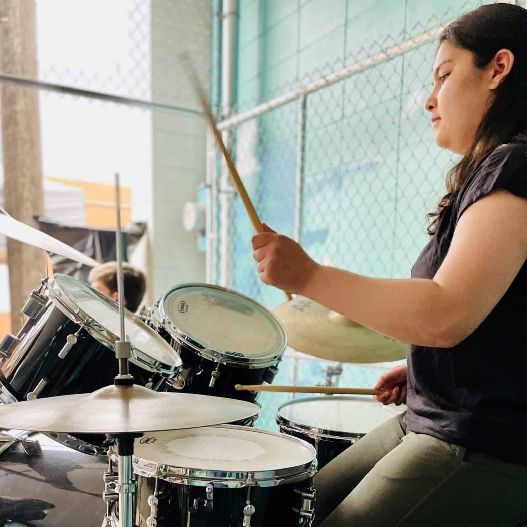 Shambhavi Pachauri, drum student Teenage girl with long black hair plays drums at an outdoor back alley Rock Show.